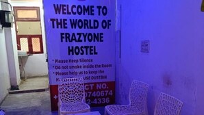 Intérieur d'une auberge de jeunesse avec une enseigne indiquant : « Bienvenue dans l'univers de l'auberge Frazyone » et un numéro de téléphone. On peut voir au premier plan des chaises en plastique et une table.