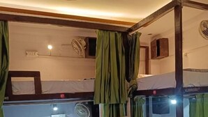Une chambre avec un lit superposé, des rideaux verts, une échelle et un ventilateur de plafond.