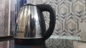 Une bouilloire en acier inoxydable avec un manche noir, portant la marque « MILTON », est posée sur une table en verre.