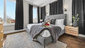 A modern bedroom with a large bed, a bedside table, a nightstand, and a window with curtains.