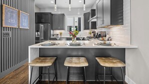 A modern kitchen with a central island, bar stools, and pendant lighting.