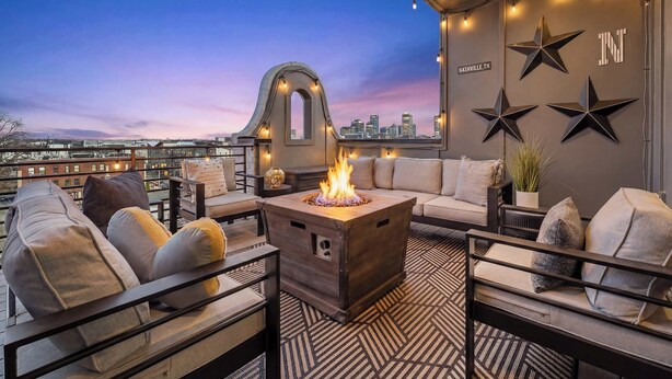 A rooftop terrace with a fire pit, seating area, and city skyline view.