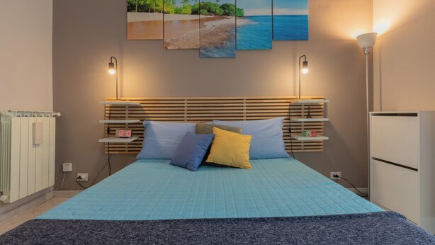 Een slaapkamer met een bed, nachtkastjes, een radiator en een schilderij van een zandstrand.