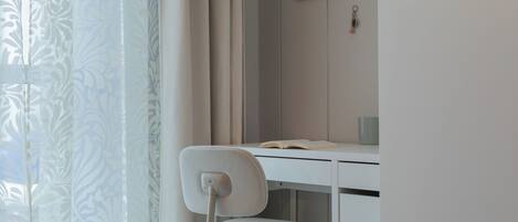 Une chambre à coucher avec un lit, un bureau avec une chaise, une fenêtre avec des rideaux et un tableau au mur.