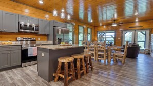A spacious kitchen with grey cabinets, stainless steel appliances, and wooden stools. - Indoor Pool, Game Room, Theater, Hot Tub & Views Near Dollywood | Crimson Crest (Sevierville)