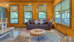 A wooden cabin interior with a brown leather sofa, two windows, a wooden coffee table, and a patterned rug. - Indoor Pool, Game Room, Theater, Hot Tub & Views Near Dollywood | Crimson Crest (Sevierville)