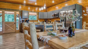A wooden interior with a dining table set for two, a kitchen with modern appliances, and a large wooden door. - Indoor Pool, Game Room, Theater, Hot Tub & Views Near Dollywood | Crimson Crest (Sevierville)