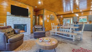 A cozy cabin interior with a fireplace, leather sofa, dining table, and a kitchen area. - Indoor Pool, Game Room, Theater, Hot Tub & Views Near Dollywood | Crimson Crest (Sevierville)