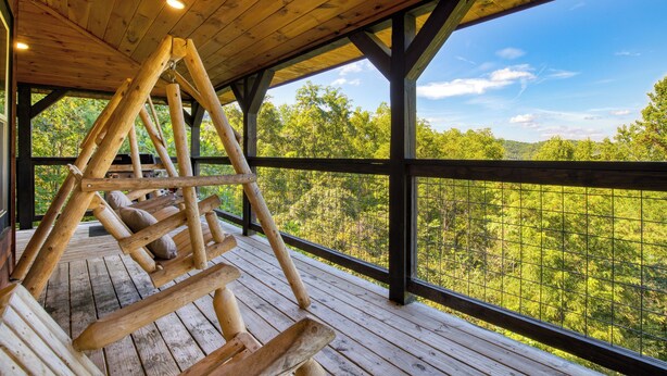 A wooden deck with a wooden swing set, large windows, and a view of a forested area. - Indoor Pool, Game Room, Theater, Hot Tub & Views Near Dollywood | Crimson Crest (Sevierville)