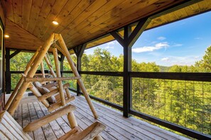 A wooden deck with a wooden swing set, large windows, and a view of a forested area. - Indoor Pool, Game Room, Theater, Hot Tub & Views Near Dollywood | Crimson Crest (Sevierville)