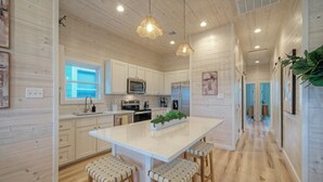 A modern kitchen with wooden cabinetry, a central island with stools, and pendant lighting. - 2 Homes, Sleeps 22 | 2 Private Pools, Firepit, Steps to Beach Boardwalk Access (Port Aransas)