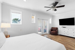 Un dormitorio con una cama, ventilador de techo, televisión, cómoda y una silla.