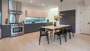 Eine moderne Küche mit einer zentralen Kochinsel, Edelstahlgeräten und einem Essbereich mit Holztisch und Stühlen.