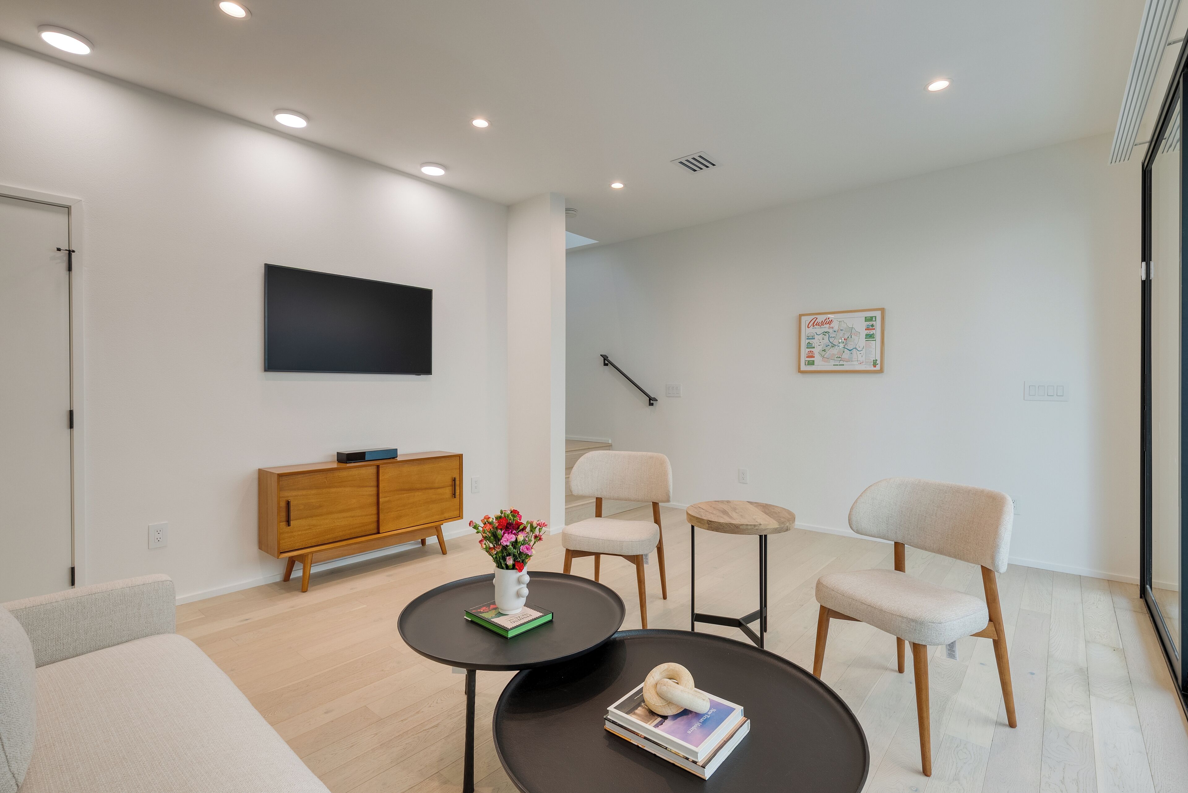 Un salon moderne comprenant un canapé, deux fauteuils, une table basse, un téléviseur, un meuble en bois et une petite table sur laquelle sont posés un vase et un livre.