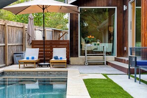 Ein Garten mit Schwimmbad, zwei Liegestühlen, einer Holzterrasse und einer überdachten Terrasse.