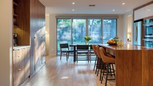 A modern kitchen with wooden cabinets, a dining area with a table and chairs, and a large window offering a view of the backyard. - 4BDR House w/ Pool & Guest House in Central Austin (Austin)