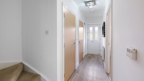 Un couloir étroit avec un plancher en bois, des murs blancs et une porte au fond.