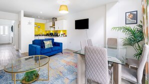 Un salon moderne avec un canapé bleu, une table basse en verre et un coin repas comprenant une table et des chaises en verre.