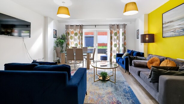 Un salon moderne avec un canapé bleu, un canapé gris, une table basse ronde et une lampe jaune.
