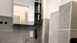 Et moderne badeværelse med en hvid vask, et spejl og en toiletpapirholder.