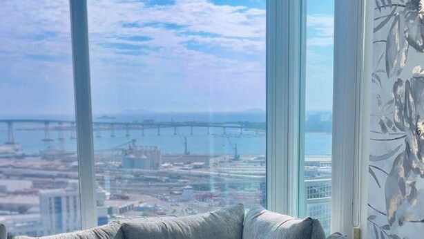 A modern living room with a large window offering a view of a bridge and cityscape. - Beautiful Two-Bedroom Escape Ocean & City Views from Every Room (San Diego)