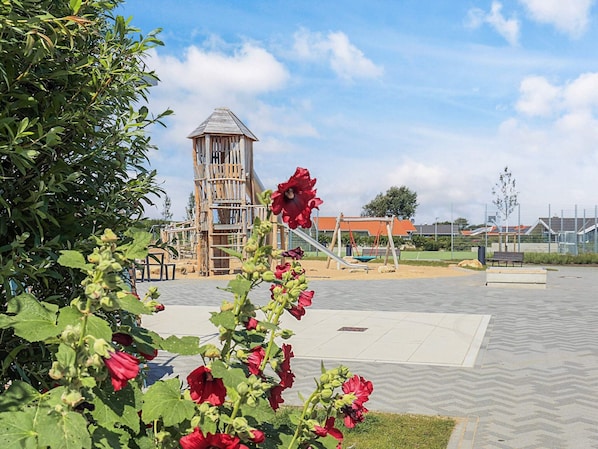 A playground with a wooden climbing structure, a swing set, and a slide. - 4 Star Holiday Home in Friedrichkoog (Friedrichskoog)