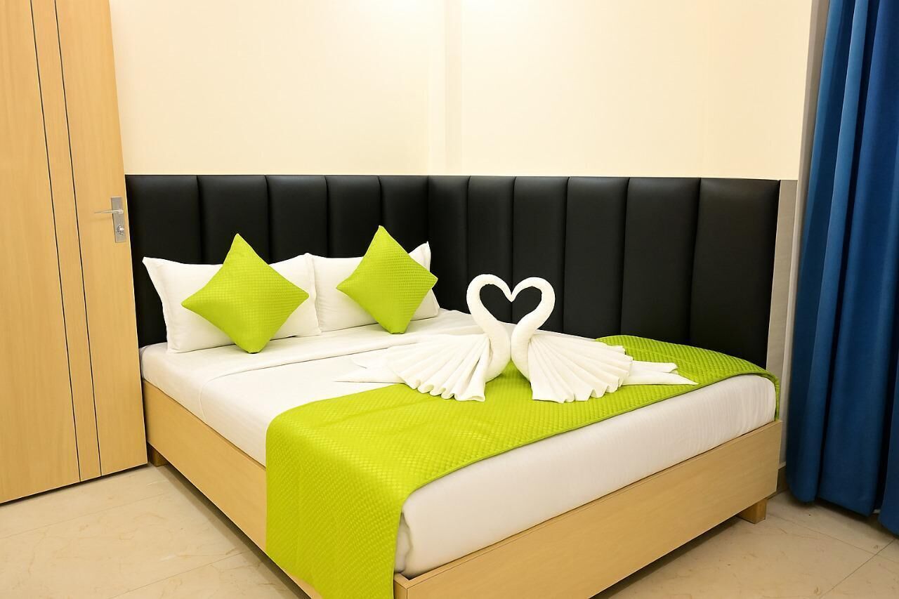 Un lit avec une tête de lit noire, une literie blanche et des coussins verts.