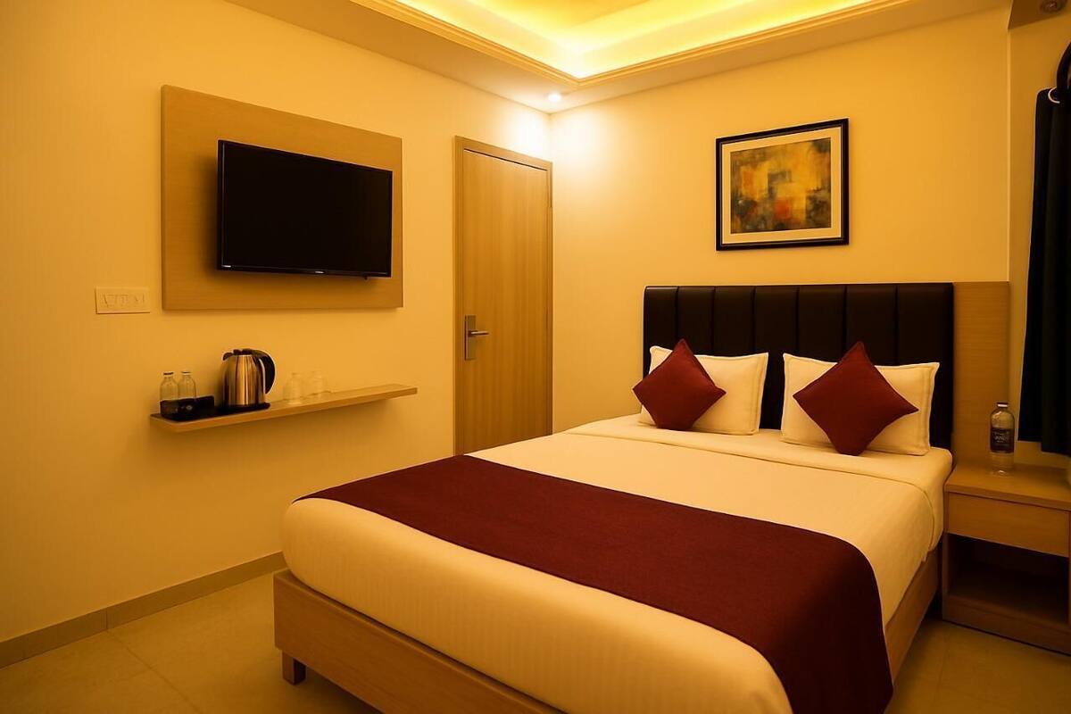 A hotel room with a large bed, a mounted TV, a painting on the wall, and a small shelf with toiletries.