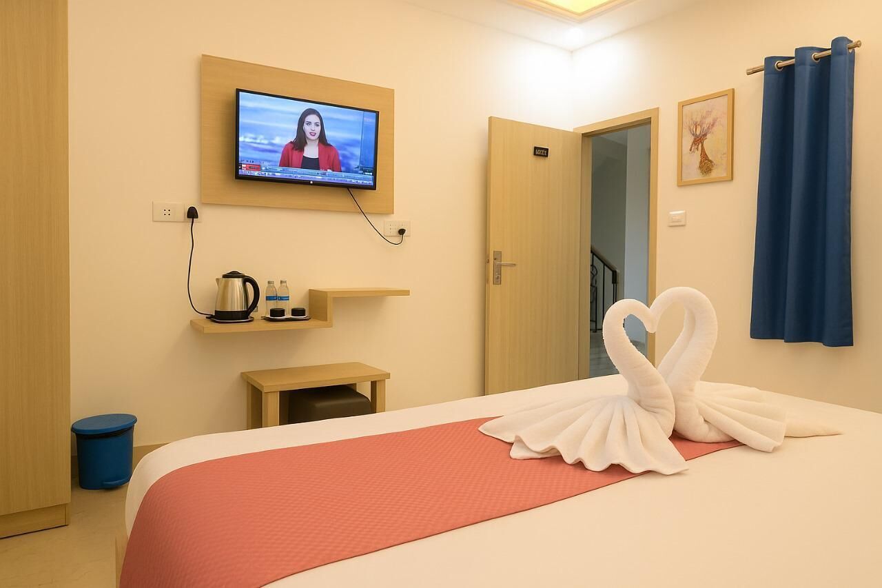 Une chambre d’hôtel avec un lit, un téléviseur fixé au mur, une petite table avec une bouilloire et une poubelle bleue.