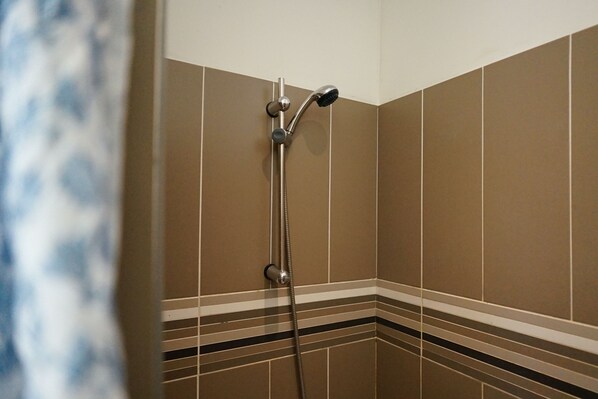 Ducha con cabezal de ducha de mano y grifo empotrado en la pared. El área de la ducha tiene paredes de azulejos marrones con franjas horizontales blancas y negras.