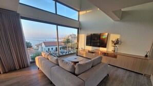 A modern living room with a large sofa, a round coffee table, and a TV mounted on the wall.