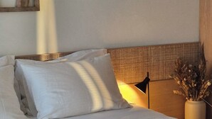 A neatly made bed with white linens, a woven headboard, and a vase with dried flowers on a bedside table.