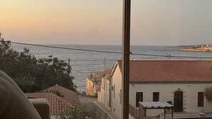 A room with a large window overlooking a coastal view, featuring a street with buildings and a clear sky.