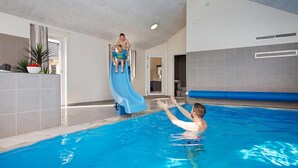 Ein Hallenbad mit einer blauen Rutsche, einer Person im Wasser und einer weiteren Person, die auf der Rutsche steht.