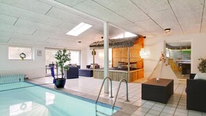 Ein moderner Innenbereich mit Schwimmbad, einer Lounge, einem mit Strohdach versehenen Bett und einem Essbereich.