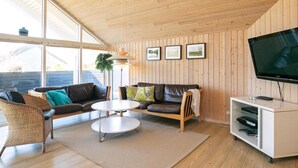 Un salon moderne avec des murs en bois, un grand téléviseur et un coin salon confortable comprenant un canapé et des fauteuils.