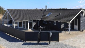 Un bâtiment moderne doté d’un toit en pente, de grandes fenêtres et d’un espace extérieur aménagé avec des sièges.