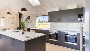 Une cuisine moderne dotée d’un îlot central, d’appareils électroménagers en acier inoxydable et d’une grande fenêtre offrant une vue sur l’extérieur.