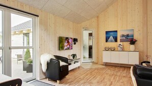 A room with wooden walls, a black leather sofa, a white cabinet, and a TV mounted on the wall.