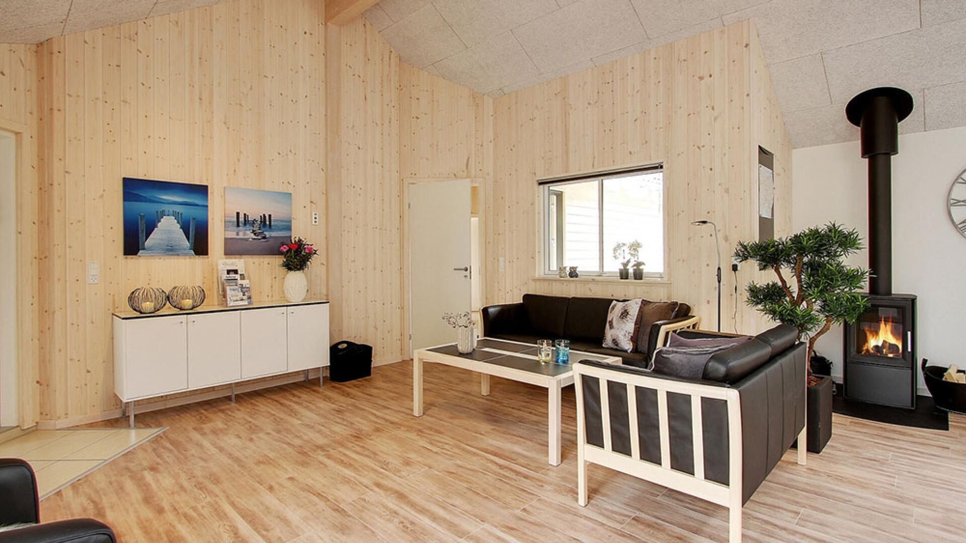 A cozy living room with wooden walls, a black leather sofa, a white cabinet, and a wood-burning stove.
