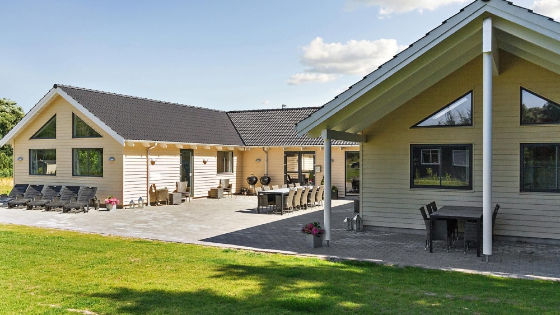 Ein zweistöckiges Haus mit einer Terrassenanlage, Sitzgelegenheiten im Freien und einem überdachten Bereich.