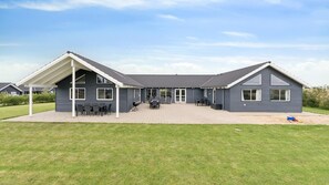 A modern two-story house with a covered patio area, a barbecue setup, and a well-maintained lawn.