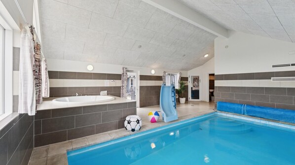 An indoor swimming pool with a slide, a jacuzzi, and a changing room with towels.