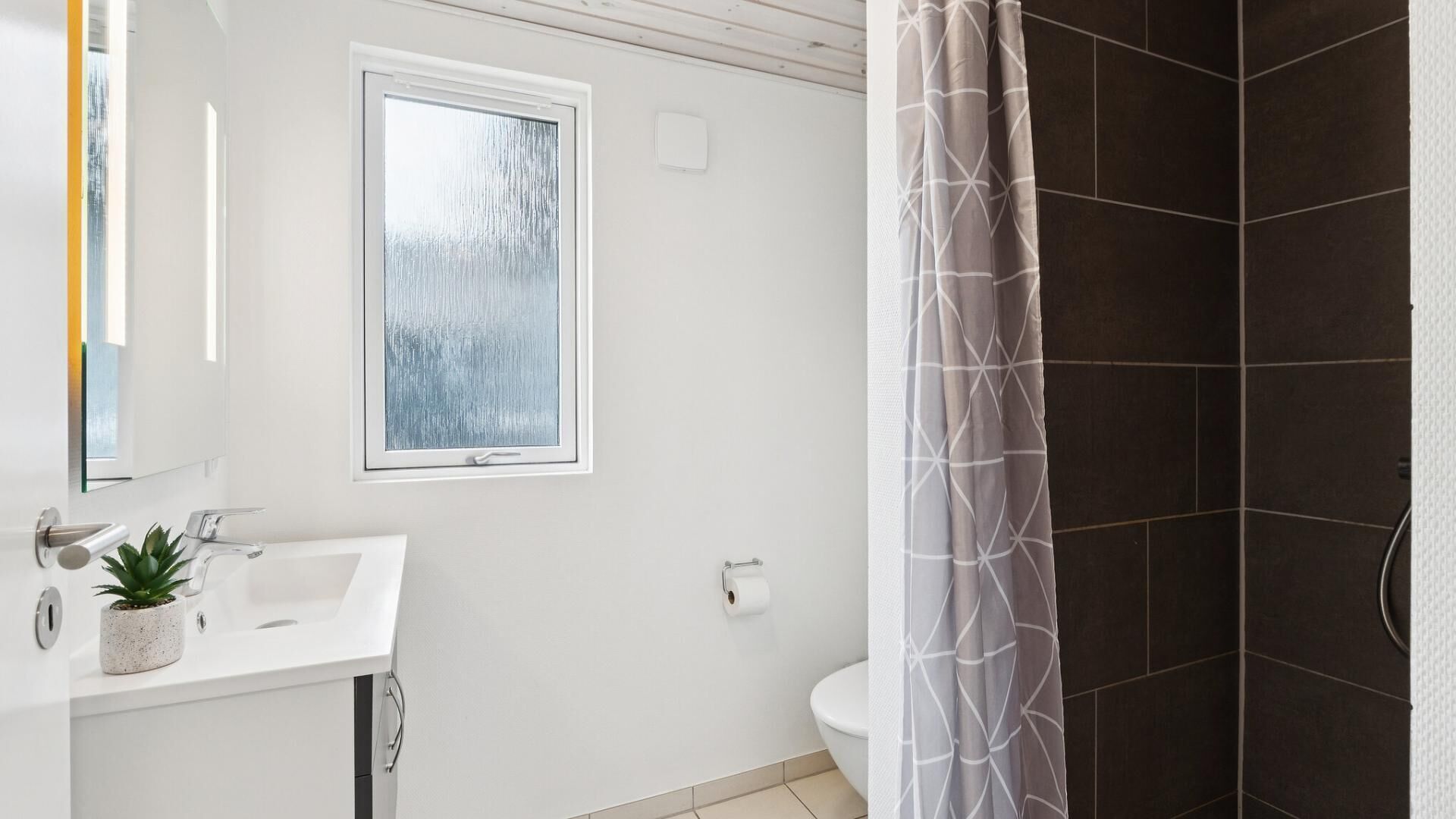 A bathroom with a white sink, a window, a toilet, and a shower area.