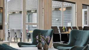 A cozy outdoor seating area with green upholstered chairs and a table, featuring a view of a building with a tiled roof.
