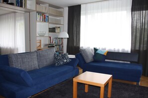 A living room with two blue sofas, a wooden coffee table, and a bookshelf filled with books.