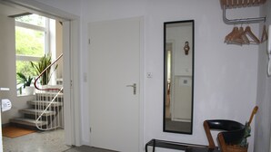 A room with a white door, a mirror, a chair, a wicker basket, and a staircase with a metal railing leading to a window.