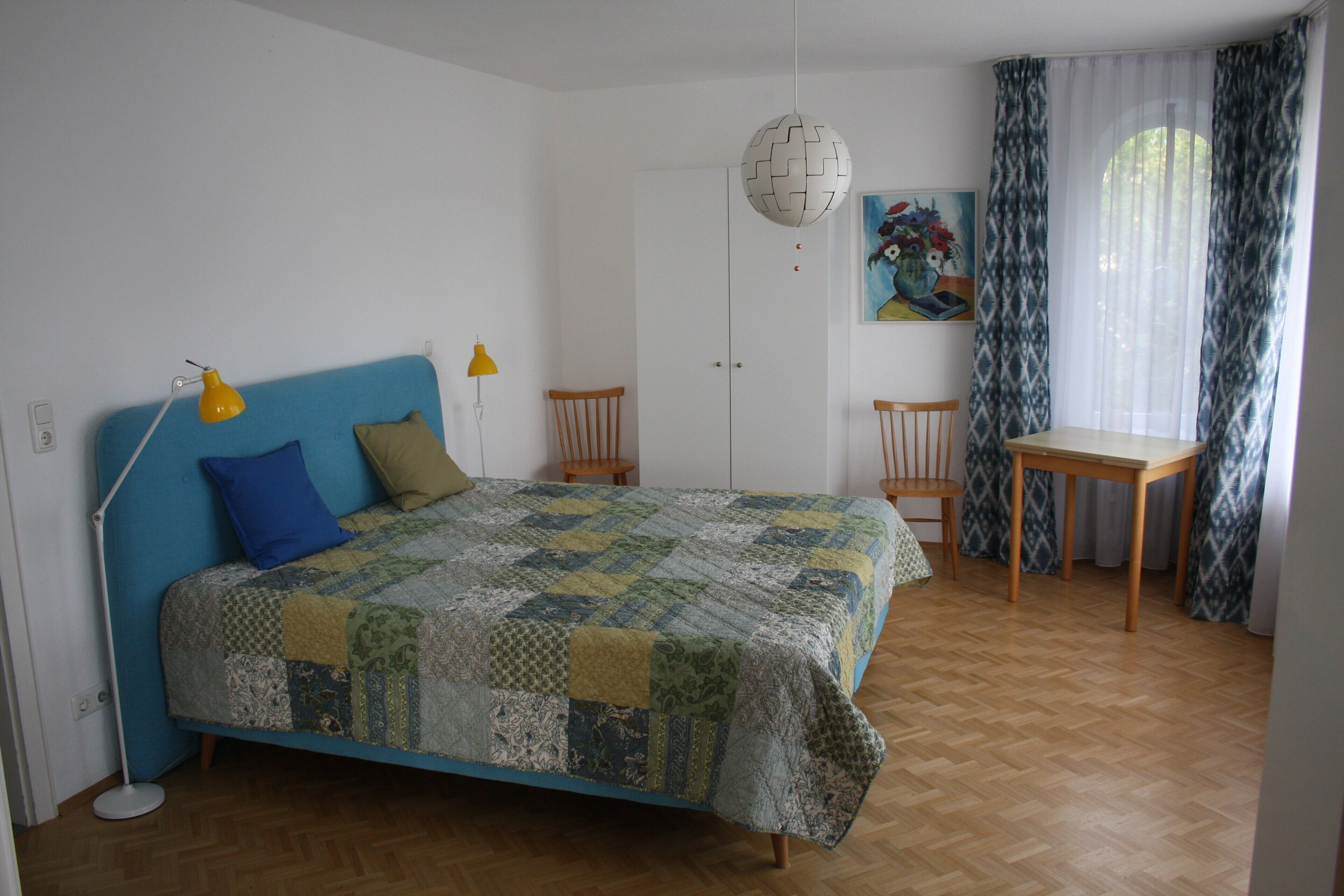 Ein Schlafzimmer mit einem Bett, Schreibtisch, Stühlen, einer Lampe und einem Bild an der Wand.