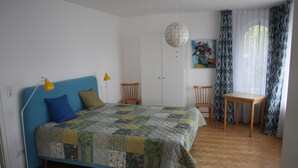 A bedroom with a bed, a desk, chairs, a lamp, and a painting on the wall.
