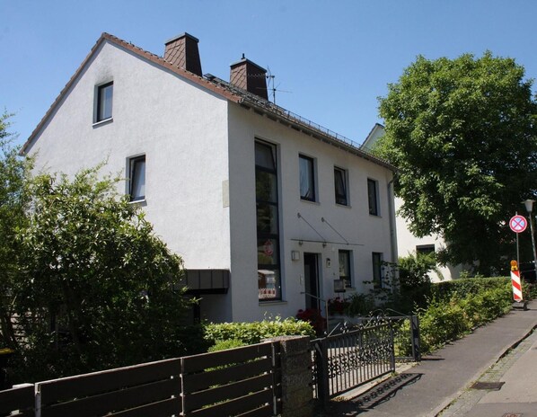 A two-story building with a white facade, a visible entrance, and a gated driveway.